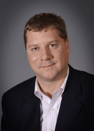 Investment advisor Daniel Gould smiling in a professional blue suit in Overland Park, KS office.